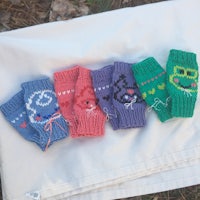five knitted fingerless mitts are laid out on a blanket