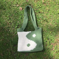 a green and white crocheted yin yang bag laying on the grass