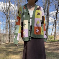 a woman is standing in the woods wearing a colorful cardigan