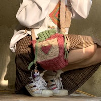 a girl sitting on the ground with a knitted bag