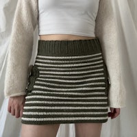 a woman wearing a white sweater and green striped skirt