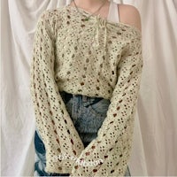 a woman wearing a crocheted sweater and denim shorts